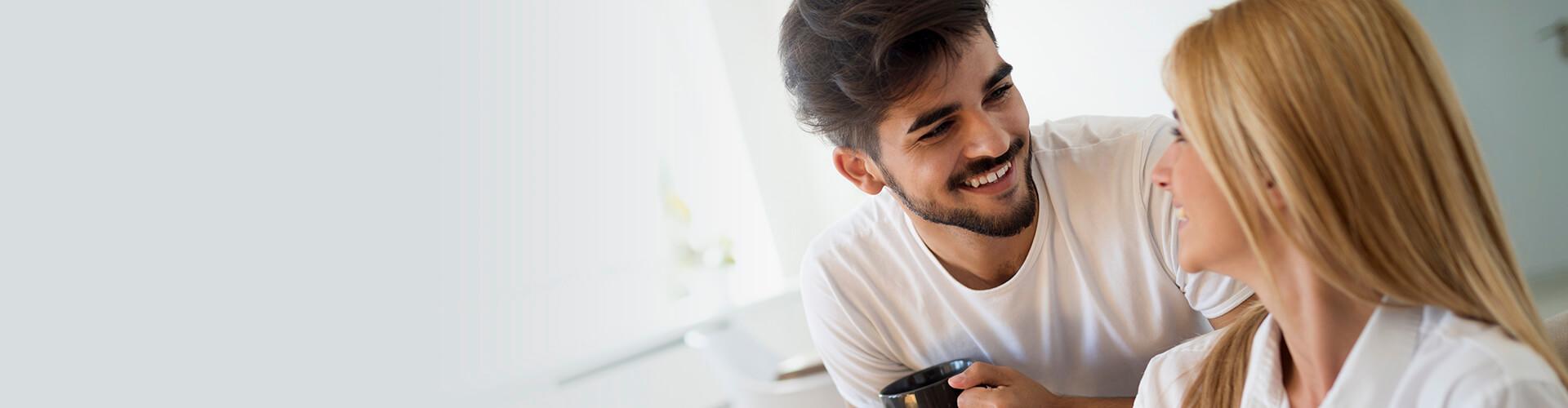 Seguros de Ahorro - Pareja joven feliz y enamorados en pijama, utilizando la tablet tumbados en el sofa de casa buscando seguros de ahorro