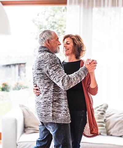 Momento Preparar mi jubilacion - Pareja senior sonriendo mientras que bailan en el salon de su casa