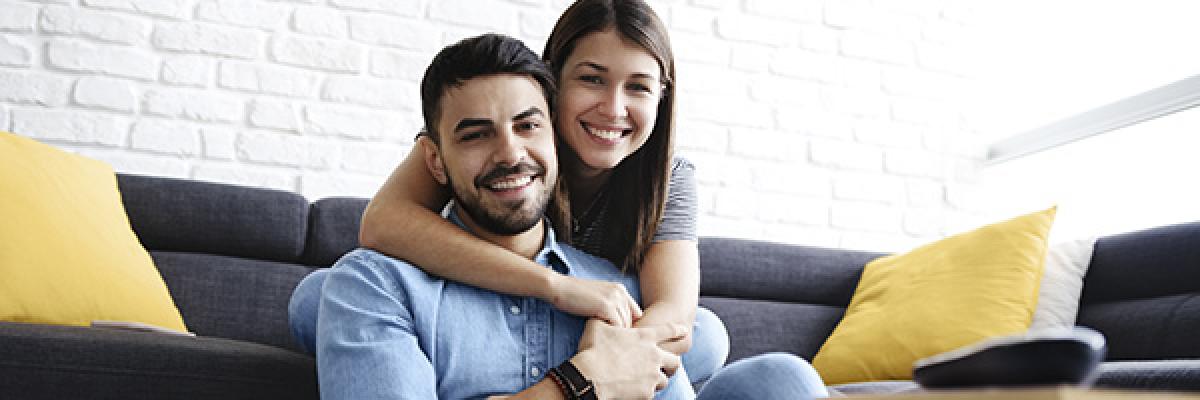 Seguro de Accidentes RGAProtección Accidentes - Pareja joven sonriendo en el salón de su casa con portátil Seguro de Accidentes RGAProtección Accidentes - Pareja joven sonriendo en el salón de su casa con portátil