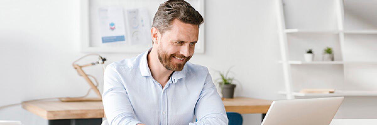Servicios para tu gestión diaria Empresas - Hombre de negocios con camisa y sonriendo mientras se encuentra trabajando con su portatil en la oficina Servicios para tu gestión diaria Empresas - Hombre de negocios con camisa y sonriendo mientras se encuentra trabajando con su portatil en la oficina