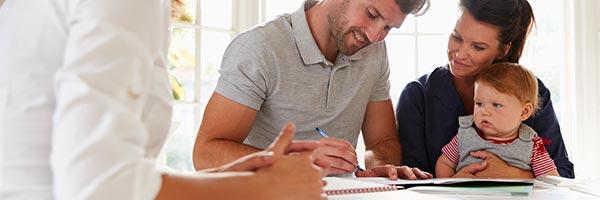 Plan de Prevision Asegurado - Familia con su bebe sonriendo y firmando un contrato de un plan de prevision asegurado en la cocina de su casa